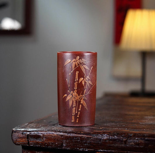 Red ceramic vase with bamboo design on a wooden surface