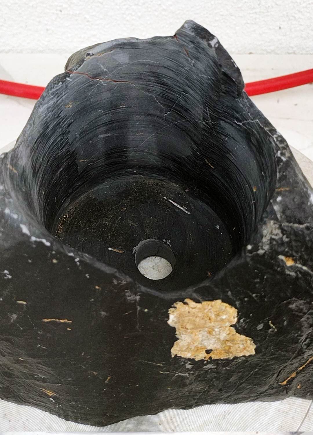 Close-up of a large black stone with a central hole, on a white background.